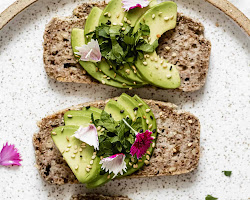 Person spreading avocado on healthy oat and flaxseed bread